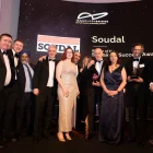 Group of formally dressed people posing on stage at an awards ceremony, with a backdrop reading 'Soudal' and 'Goldenbridge Trade & Investment Awards' behind them.