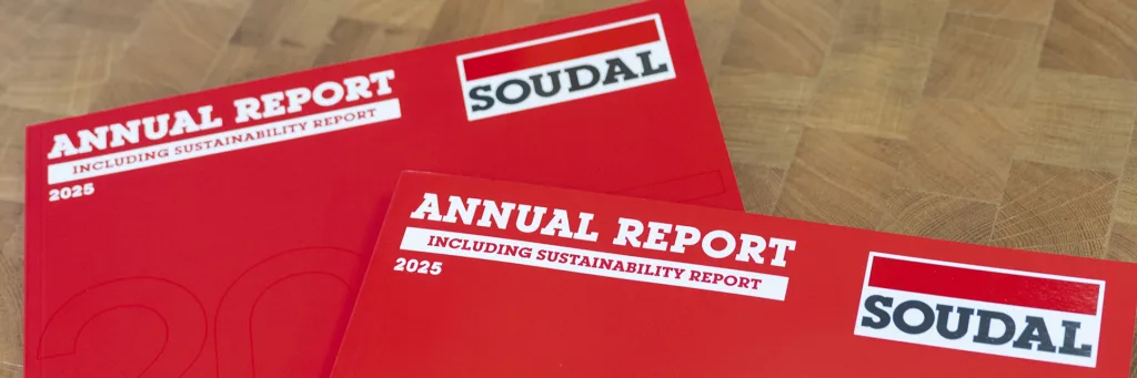 Red annual report booklets on a wooden floor, featuring bold white title text and the SOUDAL logo.